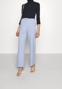 Hellblaue, weite Hose mit glatter Textur, kombiniert mit einem schwarzen Rollkragenpullover und weißen Riemchensandalen; minimalistische Gestaltung.