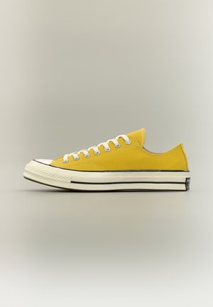 Baskets basses en toile jaune avec des lacets blancs et une semelle en caoutchouc blanche épaisse bordée de noir, vues de profil.