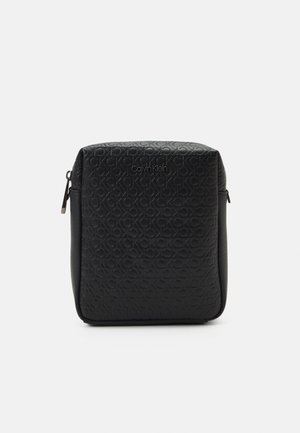 Petite pochette noire rectangulaire Calvin Klein avec motif logo CK embossé et fermeture éclair sur les côtés et le dessus.