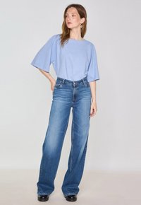 T-shirt oversize azzurro chiaro con maniche a lunghezza del gomito, abbinato a jeans a vita alta e gamba larga blu scuro e scarpe con plateau nere.