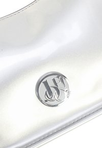 Sølvmetallic clutch med blank finish, der har en rund, sølvfarvet logo med sammenflettede bogstaver, syningsdetalje og slankt design.