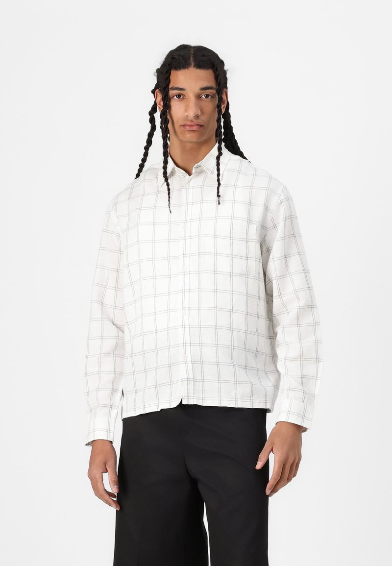 Lightly textured white button-up shirt with a black grid pattern, long sleeves, and a straight hem, paired with black trousers.