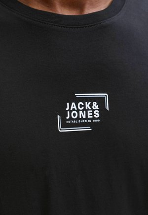 T-shirt en coton noir avec encolure ronde, arborant un logo blanc "JACK & JONES" dans un design rectangulaire et le texte "ÉTABLI EN 1990".