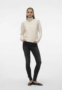 Kremasti turtleneck pulover dugih rukava, opuštenog kroja; uparen s crnim uskim farmerkama i crnim baletankama. Jednostavna zlatna lančić ogrlica.