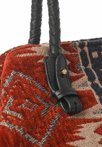 Gestreepte stoffen tas met een rode en beige geweven patroon, voorzien van zwart gevlochten leren handvatten en gouden hardware accenten.