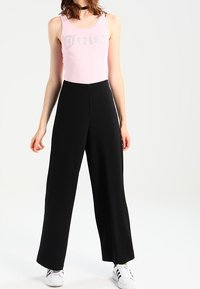 Débardeur côtelé rose clair avec le mot "Juicy" en strass, associé à un pantalon large noir taille haute et des baskets blanches.