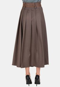 Gonna midi marrone a vita alta con ampie pieghe, cintura doppia in tessuto abbinato, indossata con scarpe nere con tacco alto.