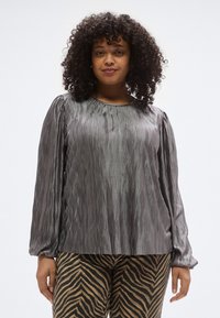 Hosszú ujjú, szürke felső, hullámos mintázatú texturált anyagból; kerek nyakkivágás, szűkített mandzsetták. Zebramintás nadrággal párosítva.