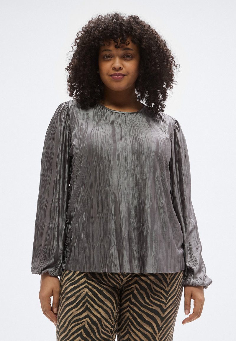 Hosszú ujjú, szürke felső, hullámos mintázatú texturált anyagból; kerek nyakkivágás, szűkített mandzsetták. Zebramintás nadrággal párosítva.