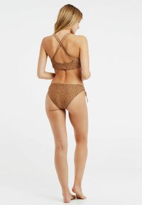 Bruine gevlekte bikini met kruisbandjes op de rug. De top heeft een ronde uitsnede, en de onderkant heeft strikjes aan de zijkanten voor een verstelbare pasvorm.