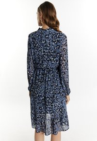 Blauw luipaardprint jurk van lichtgewicht, transparante stof. Lange mouwen, gathered taille en gerimpelde zoom zorgen voor textuur en vorm.