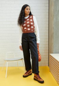 Broderad brun kortärmad tröja med vita blommor, svarta högmidjade byxor, bruna snörstövlar och en mönstrad orange väska.