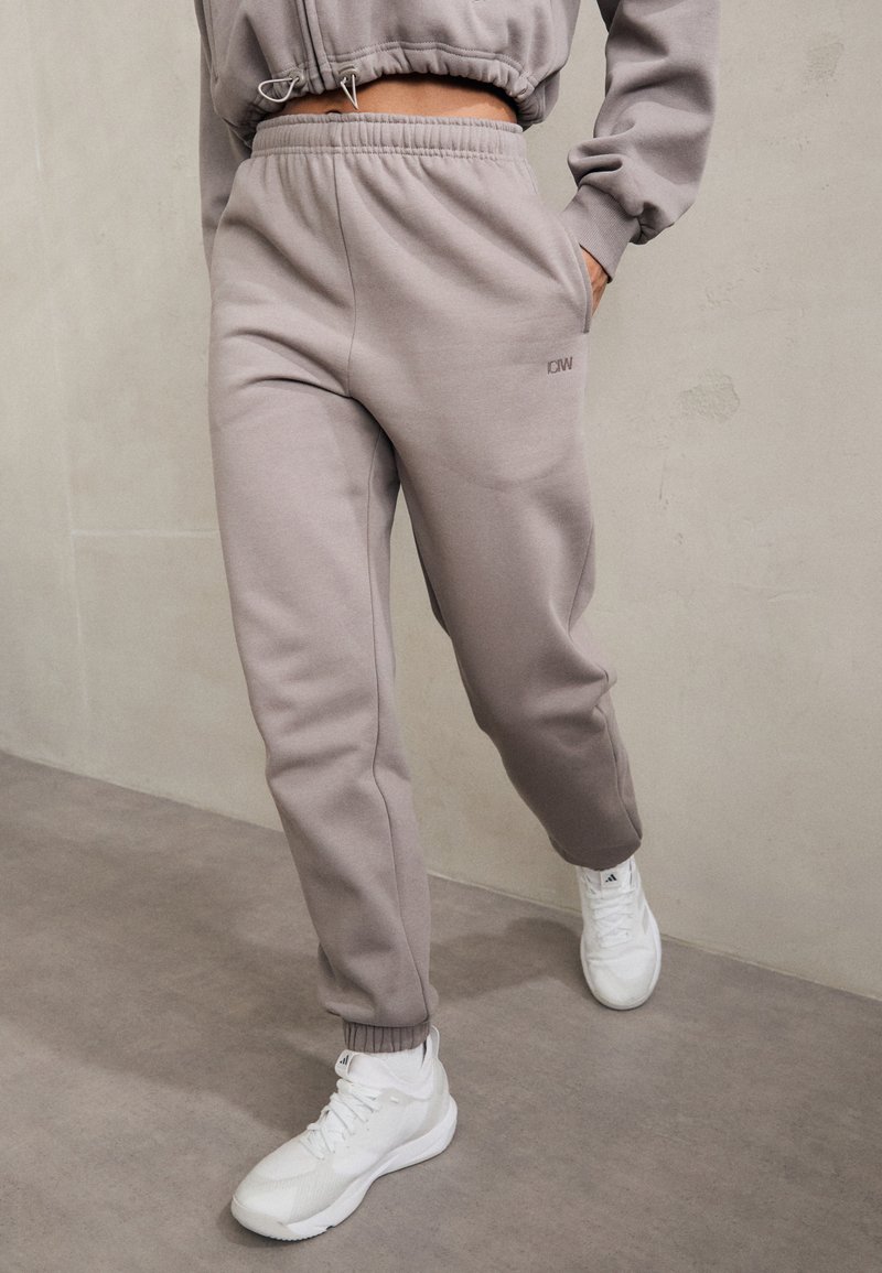 Grijze katoenen trainingbroek met een elastische tailleband en boorden, voorzien van zijzakken en een klein logo op de voorkant, gecombineerd met witte sneakers.