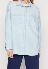 Camicia in denim azzurro chiaro con maniche lunghe, chiusura a bottoni, due tasche sul petto e un fit casual. Tessuto morbido con un aspetto leggermente sbiadito.
