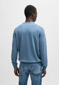 Helles, blaues Strickpullover mit langen Ärmeln, Rundhalsausschnitt sowie gerippten Bündchen und Saum, kombiniert mit verblassten blauen Jeans.