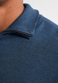 Pulover texturat albastru cu guler cu fermoar, prezentând un model ușor heather și un design ajustat, evidențiind un material moale din tricot.