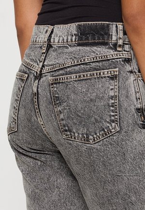 Bagfra udsigt af person iført sort top og højtaljede, falmede sorte denim jeans med lommer og synlige syninger.