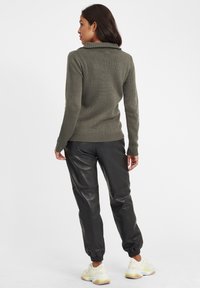 Olive green knit sweater with a high collar, paired with black leather joggers. The outfit features ribbed cuffs and elastic waistband.