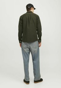 Khaki zelená košile na knoflíky se zádovou yoke detaily, spárovaná se světle modrými volnými džíny a černou obuví, z pohledu zezadu.
