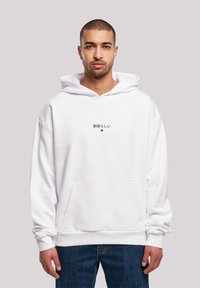 Sweat-shirt à capuche blanche avec une poche avant et un texte noir en japonais. Le tissu semble doux avec une coupe décontractée et des poignets côtelés.