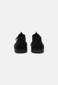 Black suede shoes with a textured sole, featuring a low cut and rear pull tab. The back displays a subtle embossed design.