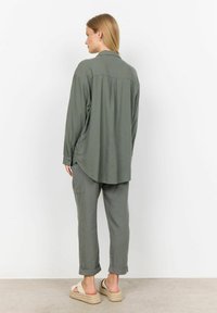 Olivgrünes, lockeres Langarmhemd, kombiniert mit passenden Hosen, mit hochgeklappten Ärmeln und lässigen Espadrilles.