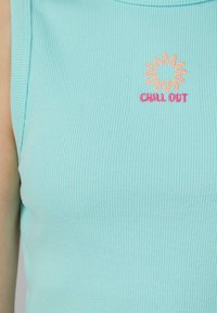Lichtblauwe geribbelde tanktop met geborduurd zonnenmotief en de tekst "CHILL OUT" in roze en oranje. Glad textuur, slim-fit ontwerp.