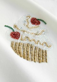 Helmeste jaapani tikand punaste kirsstega, roheliste vartidega ja langevate kuldsete helmestega valgel kangal. Tekstuurse ja värvika disainiga.