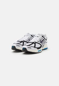 Pantofi sport albi cu accente negre și mov, din material de plasă, cu tălpi căptușite și o talpă exterioară texturată de culoare neagră. Logo-ul distinctiv Nike, în formă de swoosh.