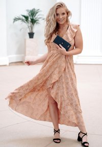 Flowing peach maxi dress with ruffled sleeves, floral pattern, and a thigh-high slit. Paired with black strappy heels and a dark clutch.