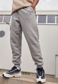 Grå svettbyxor har en figurnära design med elastisk midja och sidofickor, ihop med svarta och vita sneakers med blå detaljer.