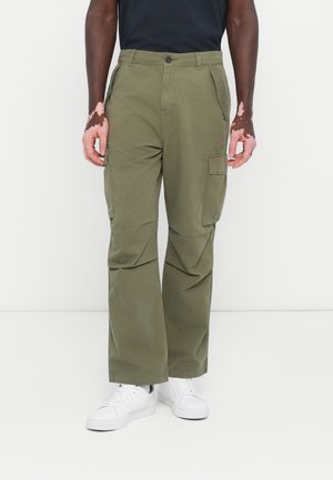 Pantalons cargo vert olive avec une coupe décontractée, dotés de plusieurs poches, d'une fermeture à bouton et d'un tissu résistant. Portés avec des baskets blanches.