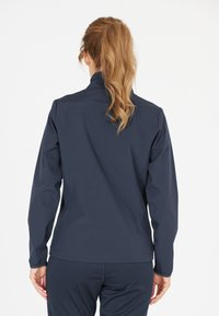 Marinblå, lättvikts-, zip-jacka med hög krage, figursydd form och elastiska ärmslut. Mjuk textur, inga synliga mönster eller metalldetaljer.