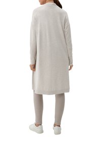 Lång, ljusgrå cardigan med ribbade muddar och nederkant, bärs över beige leggings och vita sneakers. Tyget ser mjukt och slätt ut.