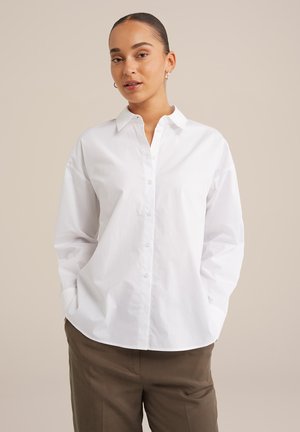 Chemise blanche à col pointu, à manches longues et à coupe décontractée. Matière en coton lisse, avec un léger éclat et sans motifs.