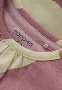 Nahaufnahme eines gestreiften Stoffes in Pink und Creme mit geraffter Naht und einem kleinen herzförmigen Knopf in der Nähe des Ausschnitts.