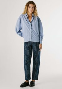 Blauw gestreepte button-up shirt met gerimpelde placket, gecombineerd met blauw patroon wijde broek met bloemontwerpen, gedragen met zwarte loafers.