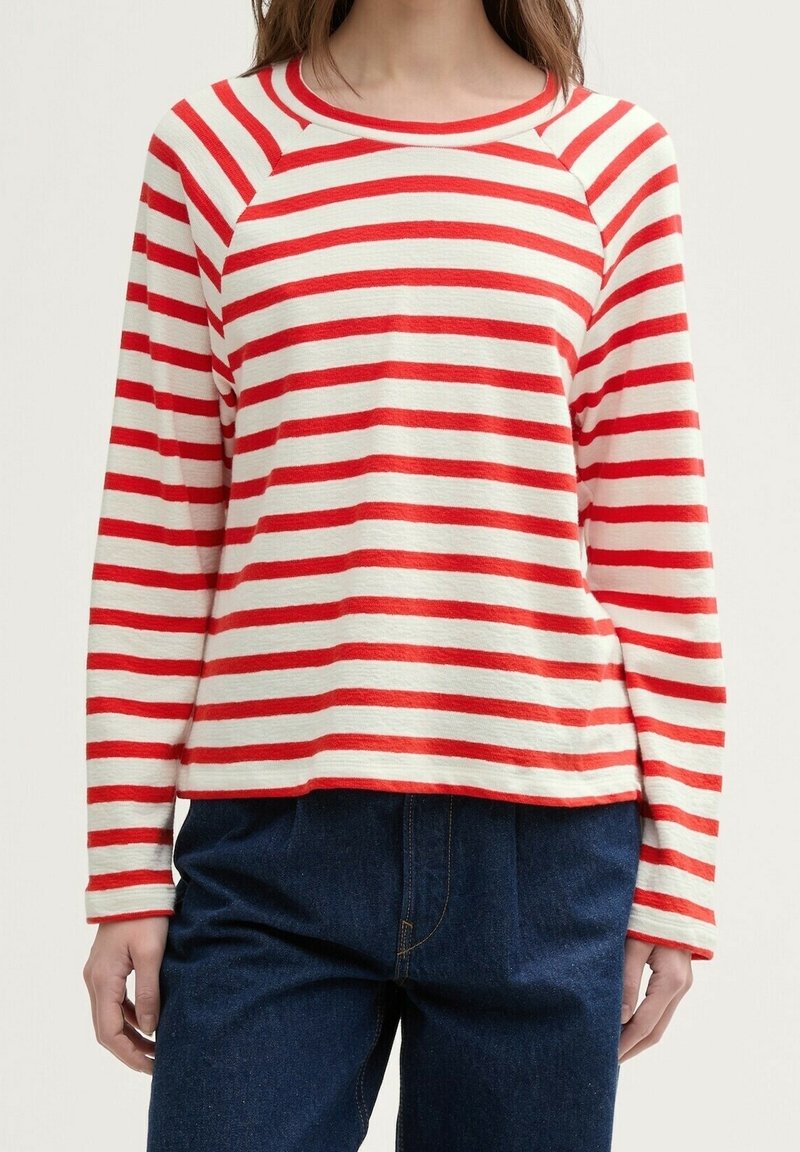 Rot und weiß gestreiftes Langarmshirt mit rundem Ausschnitt und Raglanärmeln, aus weichem Stoff. Kombiniert mit dunkelblauen High-Waist-Jeans.