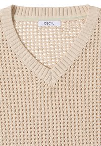 Haut beige en maille sans manches avec col en V, motif ajouré et étiquette de la marque "CECIL" à l'intérieur de l'encolure.