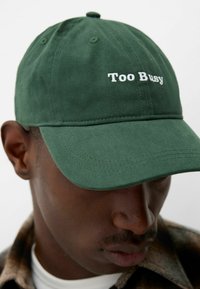 Casquette en coton verte avec le texte blanc "Trop Occupé" à l'avant, dotée d'un pic classique incurvé et d'une finition en tissu texturé.
