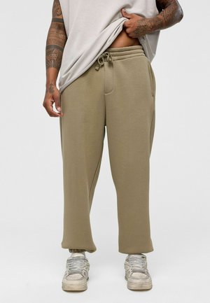 Beige katoenmix joggingsbroek met een elastische tailleband en trekkoord, voorzien van zijzakken en taps toelopende boorden. Gemaakt in combinatie met grijze sneakers.