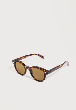 Tortoiseshell patterned round sunglasses with brown tinted lenses resting on a white surface.