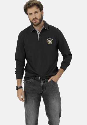 Schwarzes Langarmpolo mit grauem Kragen, mit gesticktem Logo. Kombiniert mit dunkelgrauen Jeans und einer schwarzen Uhr.