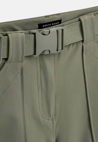 Gros plan d'un pantalon vert olive avec une ceinture intégrée réglable munie d'une grande boucle en plastique et d'une étiquette "North Sails" sur la taille.