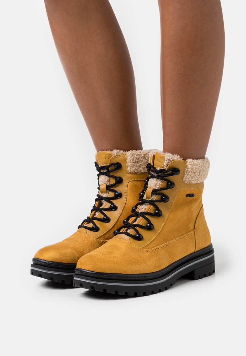 Geel suède enkellaarsjes met zwarte veters, faux bont kraag en een robuuste zwarte loopzool. Heeft een licht gewatteerde tong voor comfort.