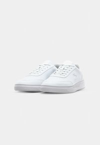 Valkoiset tennarit, jotka on valmistettu sileästä synteettisestä nahasta, teksturoidulla pohjalla, joissa on nauhat ja pienet reiät ilmanvaihtoa varten.