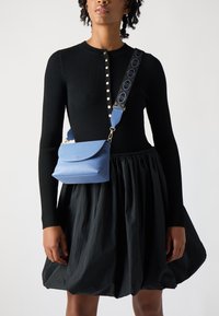 Maglietta nera a righe con maniche lunghe e dettagli in bottone, abbinata a una gonna nera ampia. Una piccola borsa a tracolla blu testurizzata con una tracolla a fantasia.