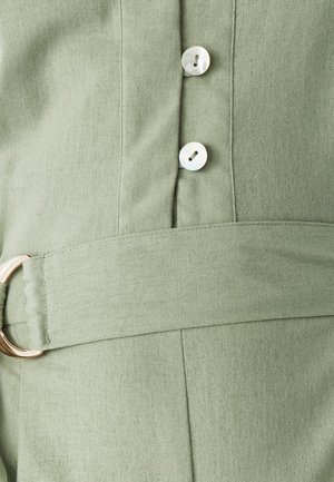 Heledad rohelisest kangast rõivas, millel on kaks valget nööpi ja sobiv riidest vöö, mis on kinnitatud kullast metallrõngaga.