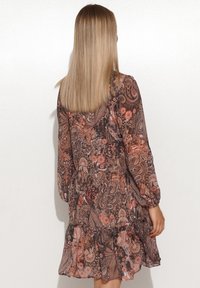 Fließendes, durchsichtiges Kleid in Braun mit floralem und Paisleymuster. Das Kleid hat lange Ärmel und einen gestuften Rüschensaum, der einen strukturierten Look schafft.