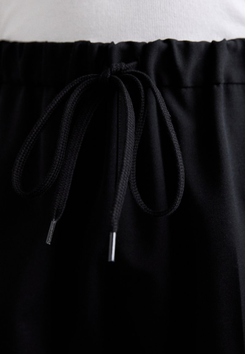 Sorte snørrebuksner med blødt, glat stof, elastisk talje og justerbar sort snor med metalender.